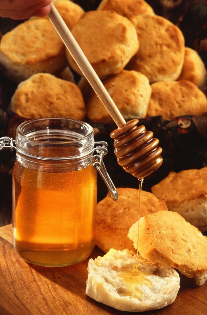 A jar of honey with a honey dipper and a slice of bread on a kitchen table