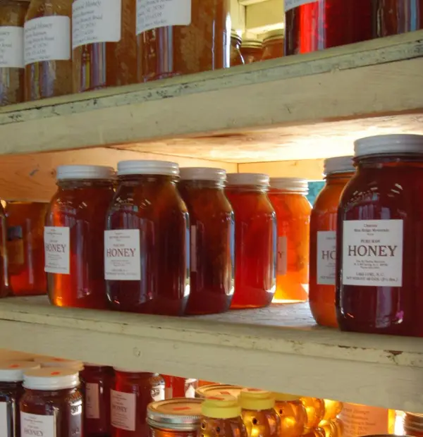 Shelves of glass jars of local honey with paper labels for sale at a farmers market stand
