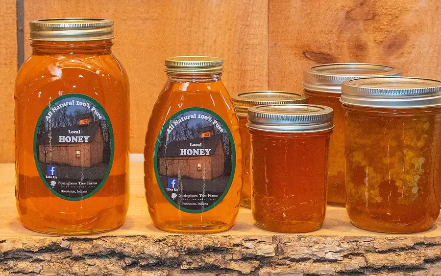 Jars of local liquid honey and a jar of chunk comb honey lined up on a wooden farm stand shelf