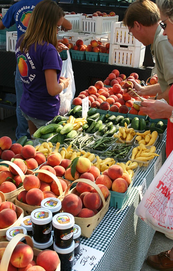 Baskets of fresh fruits and vegetables alongside homemade jelly at a farmers market stand, typical items traded for honey