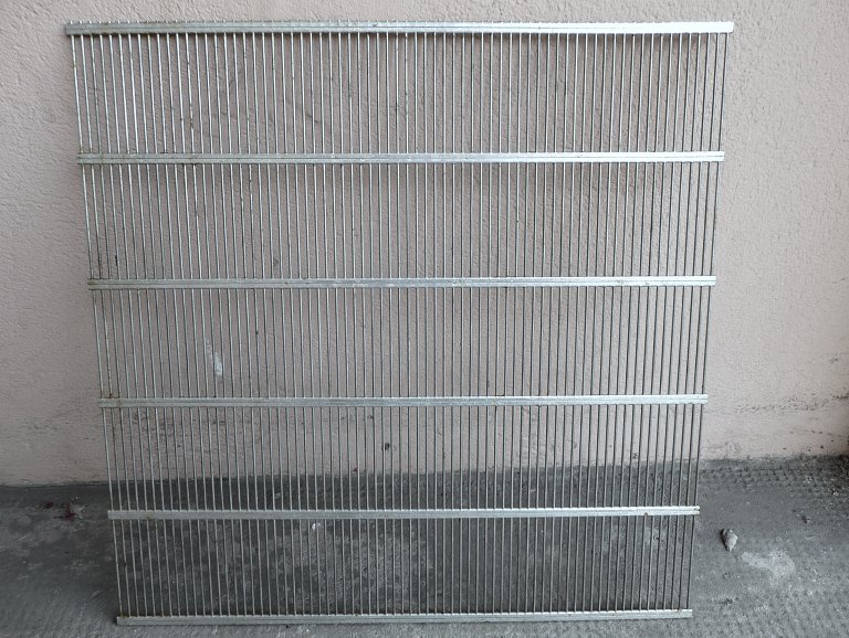 Close-up view of a queen excluder's slotted metal grid spacing
