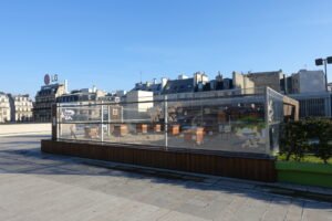 Rooftop beehives behind a glass enclosure atop a Paris building with city skyline