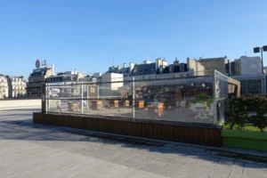 Rooftop beehives behind a glass enclosure atop a Paris building with city skyline