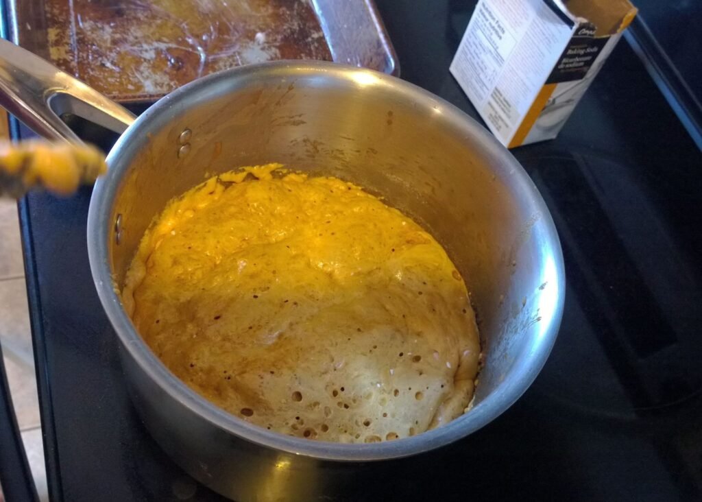 Sugar syrup bubbling up rapidly after baking soda is stirred in during honeycomb candy making