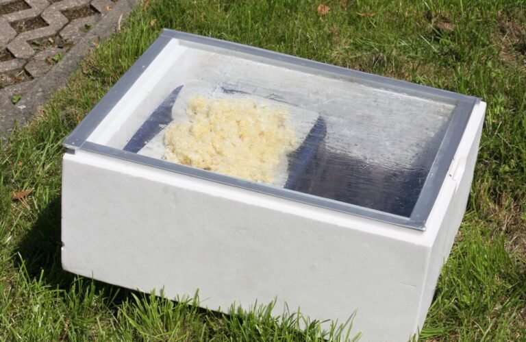 A simple insulated foam-box solar wax melter with a glass lid, cappings wax melting inside on a sunny lawn