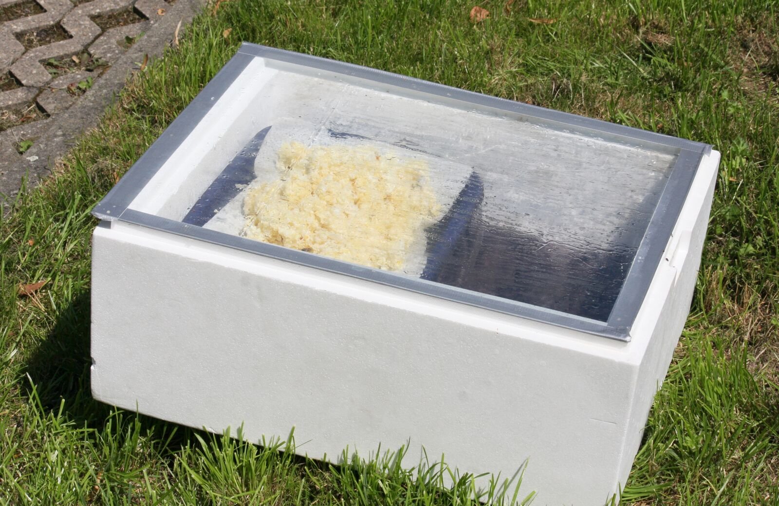 A simple insulated foam-box solar wax melter with a glass lid, cappings wax melting inside on a sunny lawn