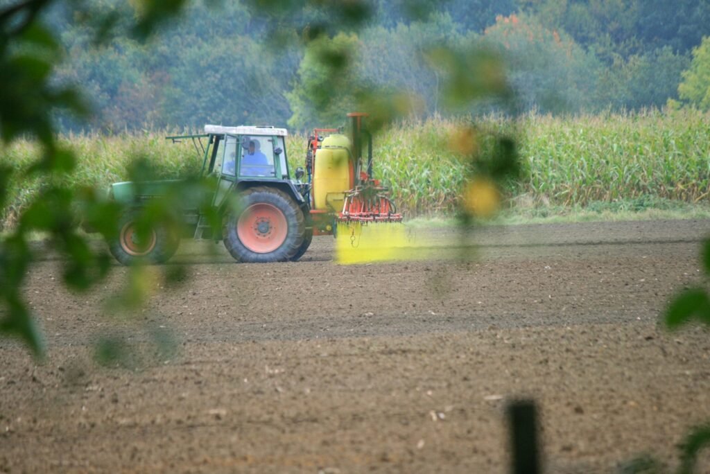 Farm tractor applying pesticide spray to a field with a boom sprayer