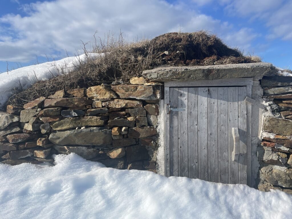 Snow-covered exterior door of a traditional underground root cellar, the cold damp storage type that is the wrong climate for honey and wax