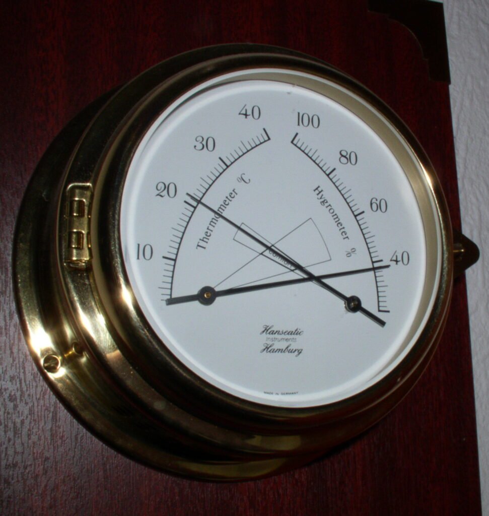 A wall-mounted thermo-hygrometer displaying both temperature and relative humidity, the kind of instrument used to monitor a honey and wax storage room