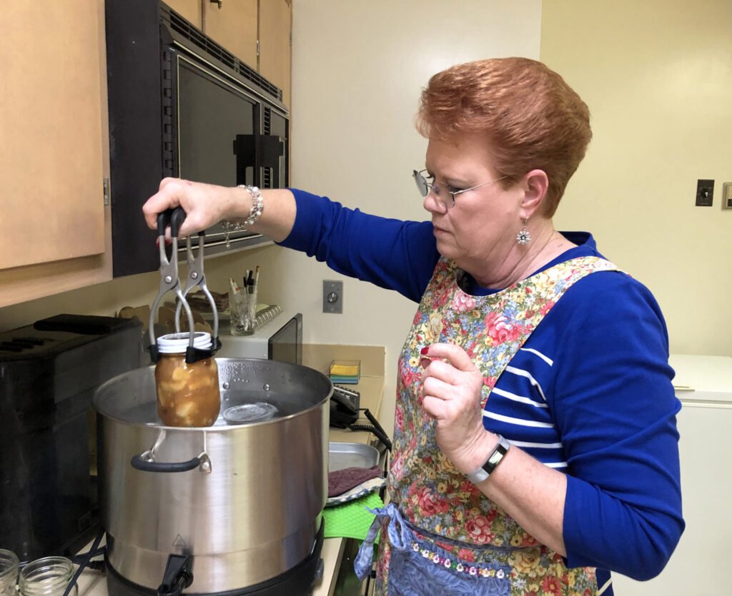Glass canning jars processing in a boiling-water bath canner on a stovetop, the method used for high-acid honey-sweetened preserves