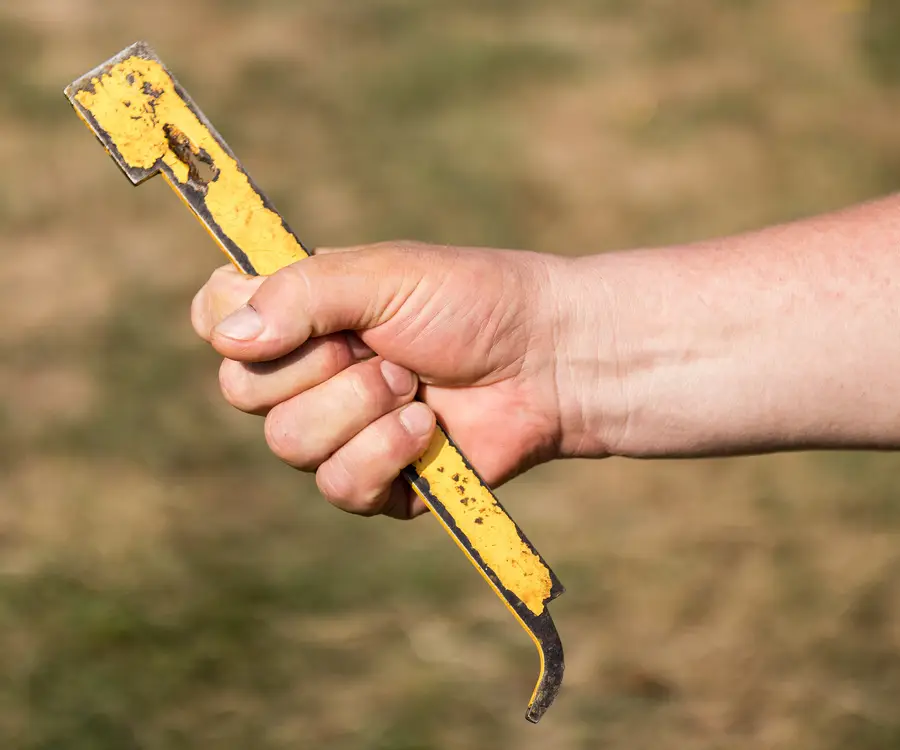 Hand gripping a worn hive tool with chipped yellow paint and a hooked end, the kind beekeepers wear out