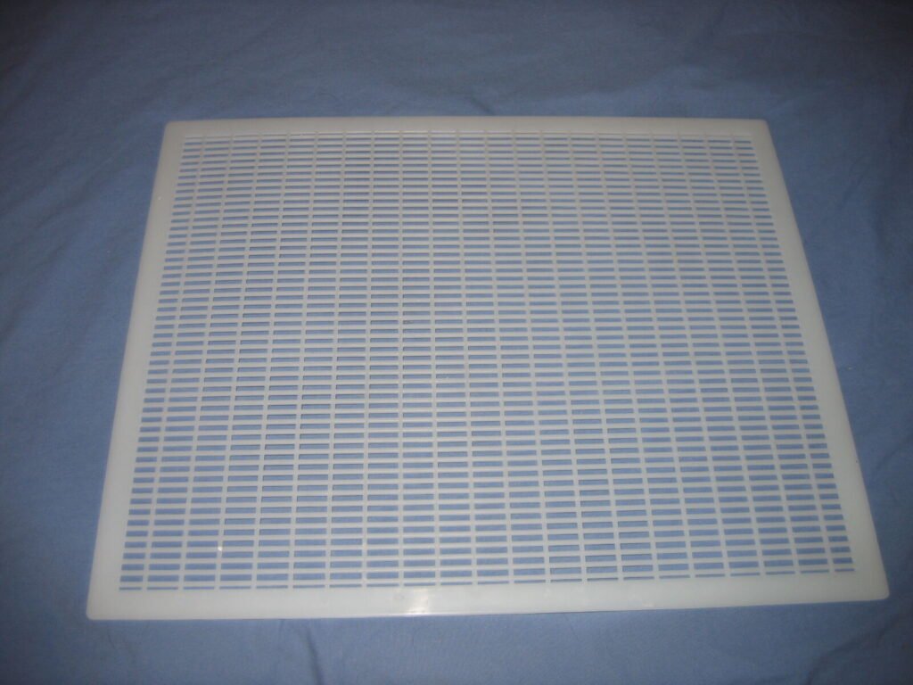 A perforated metal queen excluder photographed against a plain background