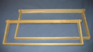 Two assembled wooden Langstroth frames, deep and medium, with wedge top bars lying flat on a blue background
