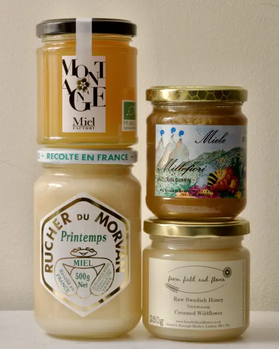 Four jars of creamed honey ranging from pale white to golden, showing the smooth, opaque look of fine-grained honey
