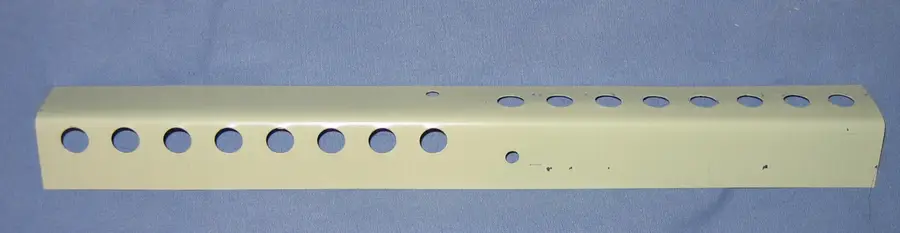 Pale green metal mouse guard strip with rows of round holes lying on a blue cloth