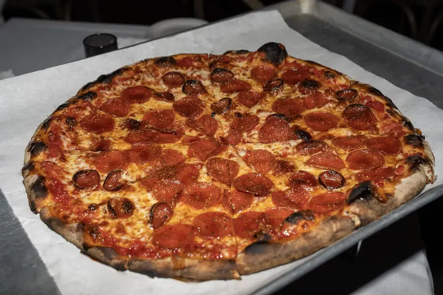 Whole pepperoni pizza with a charred crust on a baking tray lined with parchment paper at a pizzeria