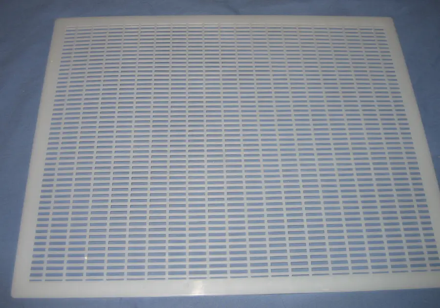 White plastic queen excluder, a flat grid of narrow slots inside a solid rim, lying on a blue cloth