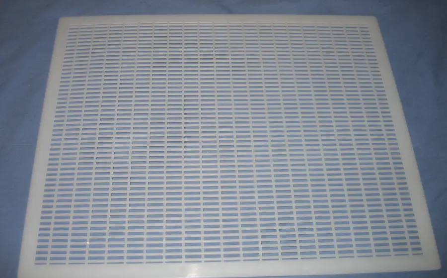 White plastic queen excluder with rows of narrow slots lying flat on a blue cloth, like the one supplied with Flow Hives